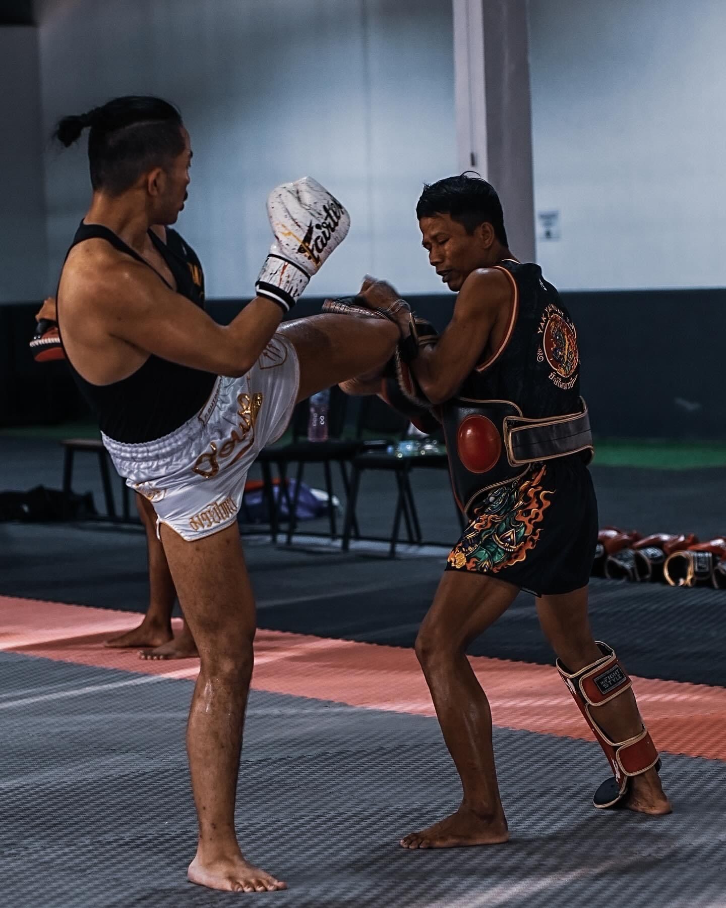 Two martial artists practicing Muay Thai with protective gear in a gym setting.