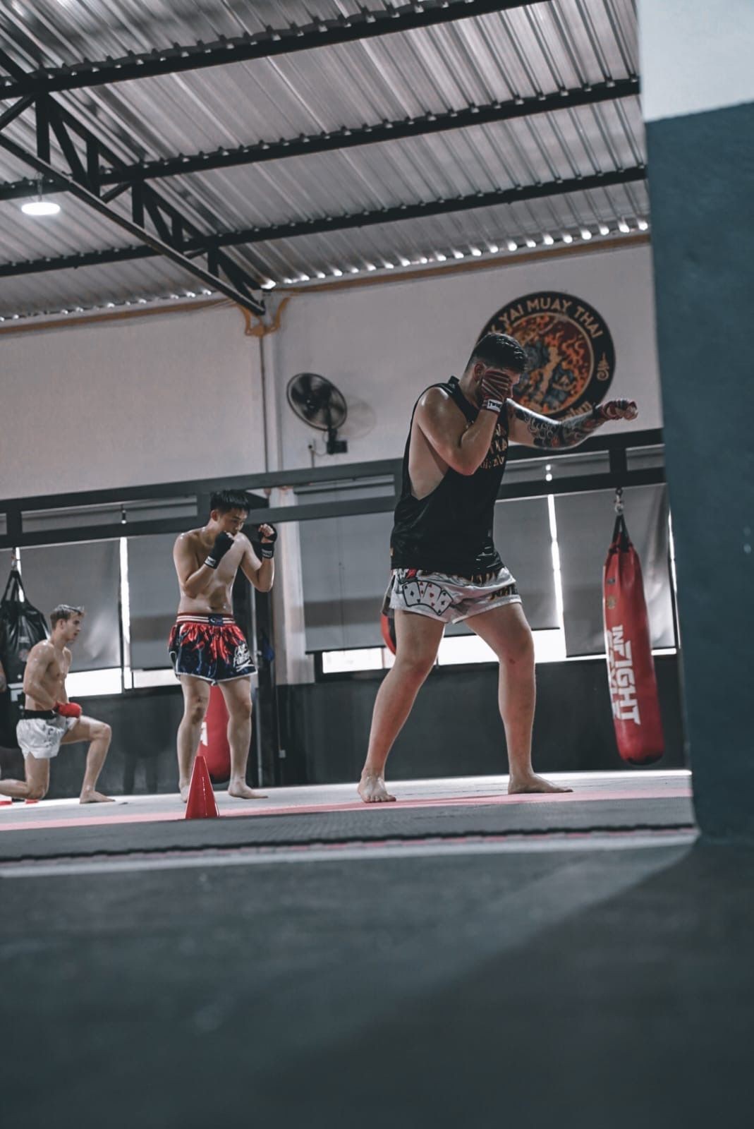 Group of people practicing Muay Thai in a gym with punching bags and boxing gloves.